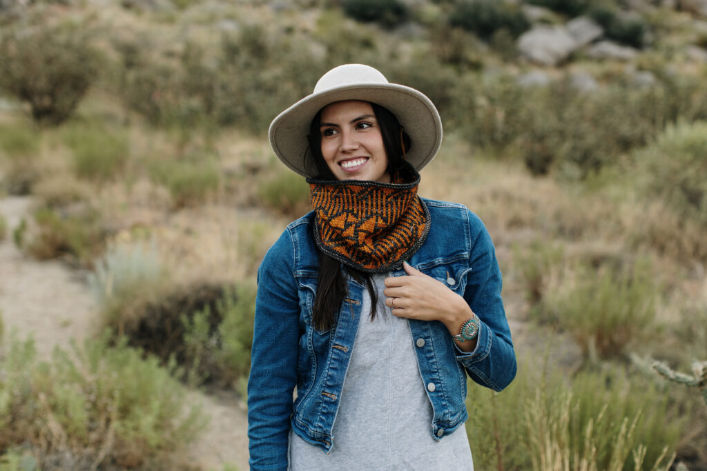 Experience the natural allure of Native American culture with this captivating image of a smiling Native American woman. Adorned in a stylish jean jacket, hat, and knitted cowl, she stands gracefully against a backdrop of the desert brush. Immerse yourself in the rich heritage and beauty of Native American tradition embodied in this radiant scene.
